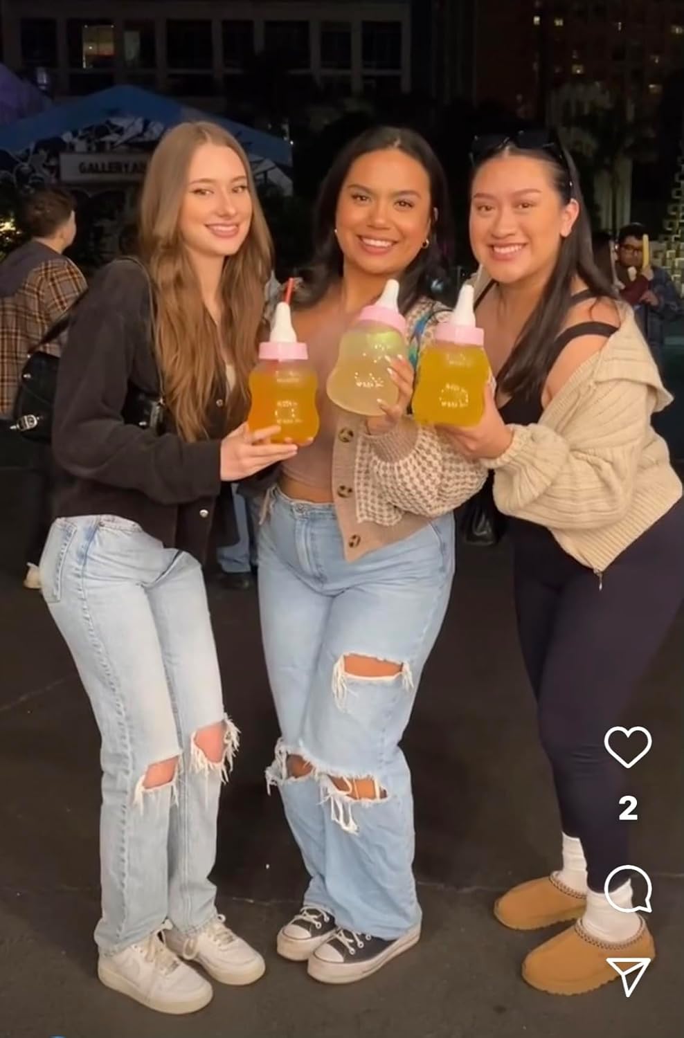 Three women holding piggy bank bottles of a mango juice at an outdoor event.